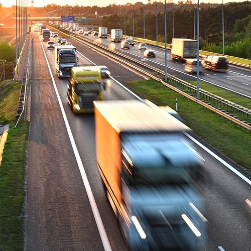 Busy highway at sunset with multiple trucks and cars traveling in both directions on a multilane road.